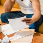 Man sitting on sofa reading unpaid bills, looking stressed and concerned over financial debt.