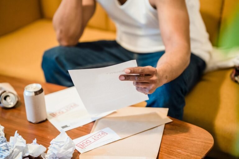 Man sitting on sofa reading unpaid bills, looking stressed and concerned over financial debt.